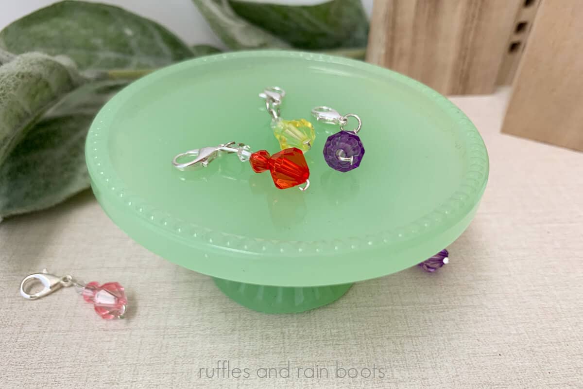 Horizontal close up image of colorful bead stitch markers on a green glass cupcake plate.