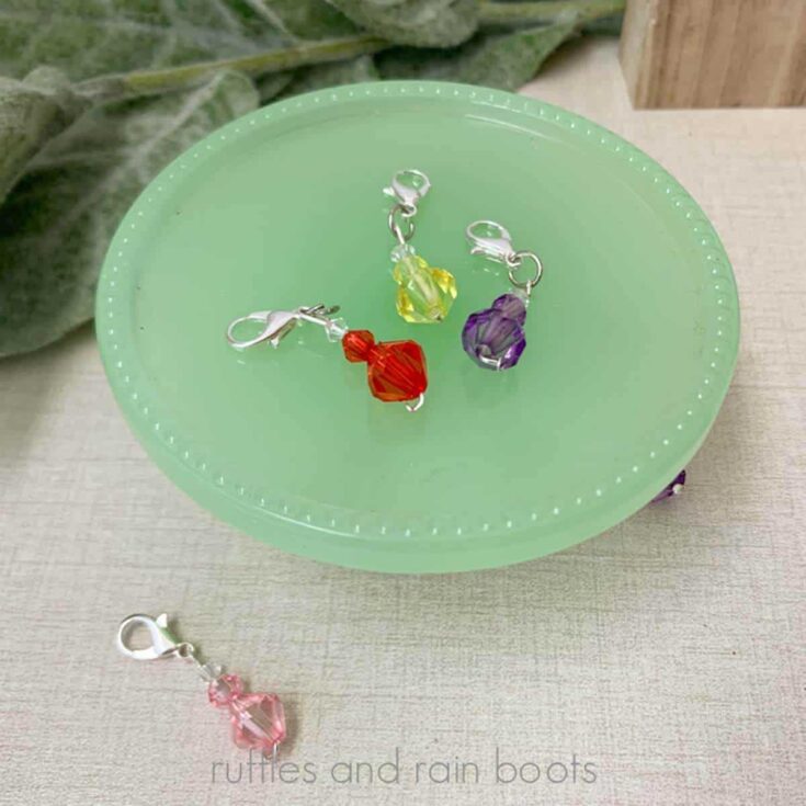 Square close up image of three beaded stitch markers on a green glass cupcake stand.