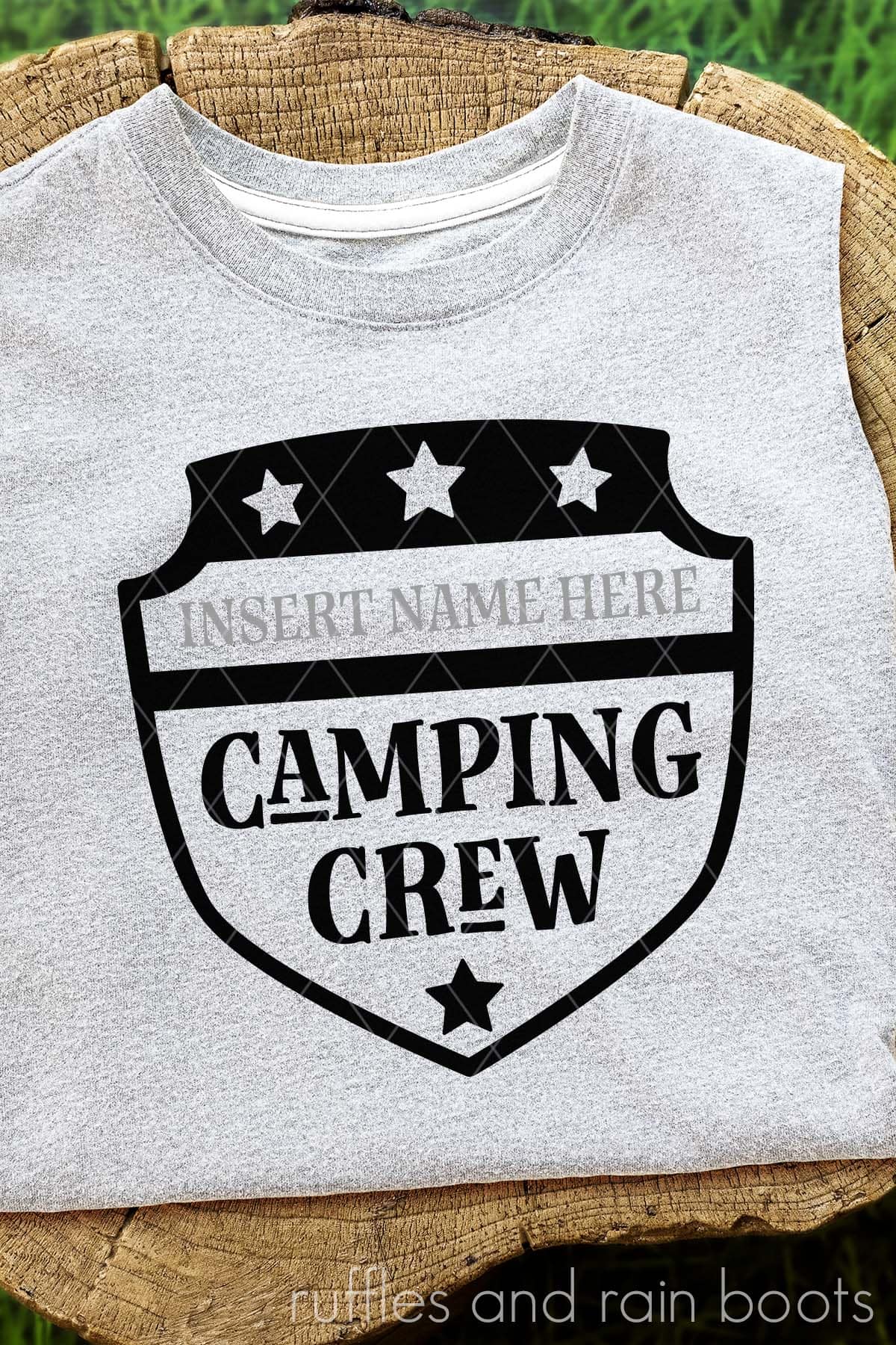 Vertical image of a badge style camping SVG with custom name area on a gray shirt placed on a stump.