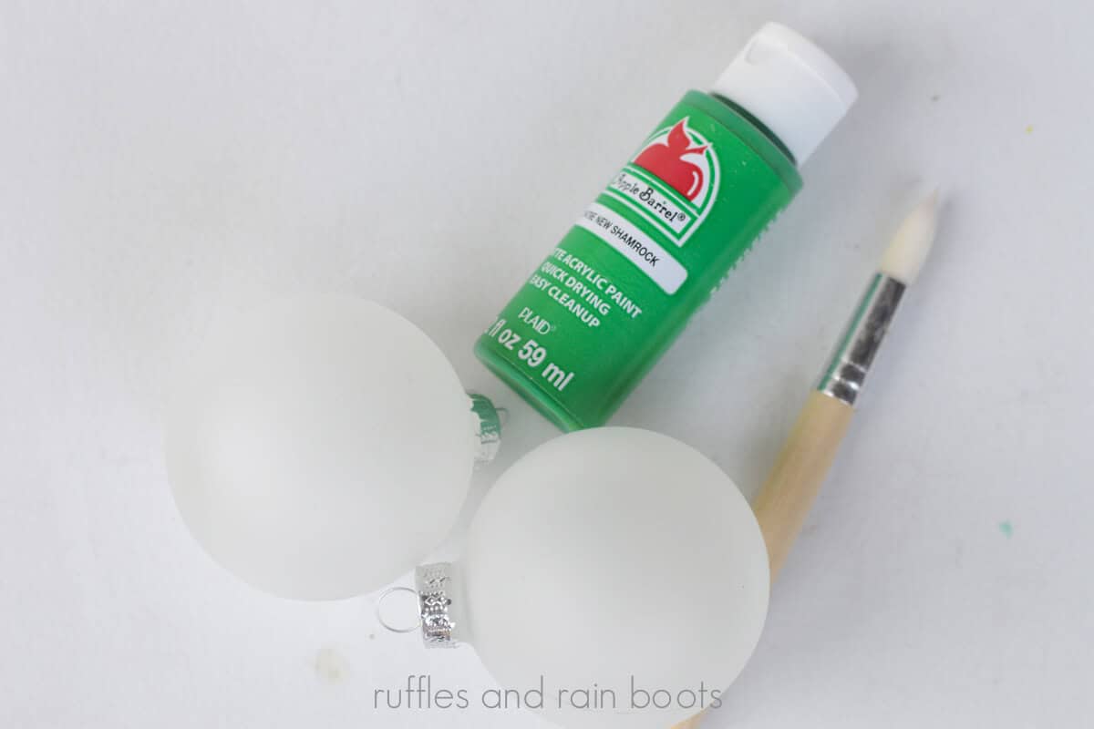 Crafter assembling what you need for this craft: paint, Christmas ornaments, and a small paint brush.