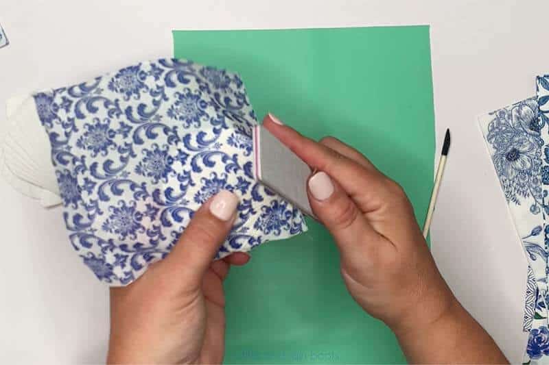 Crafter using a file to sand off the decoupaged napkin on the seashell.