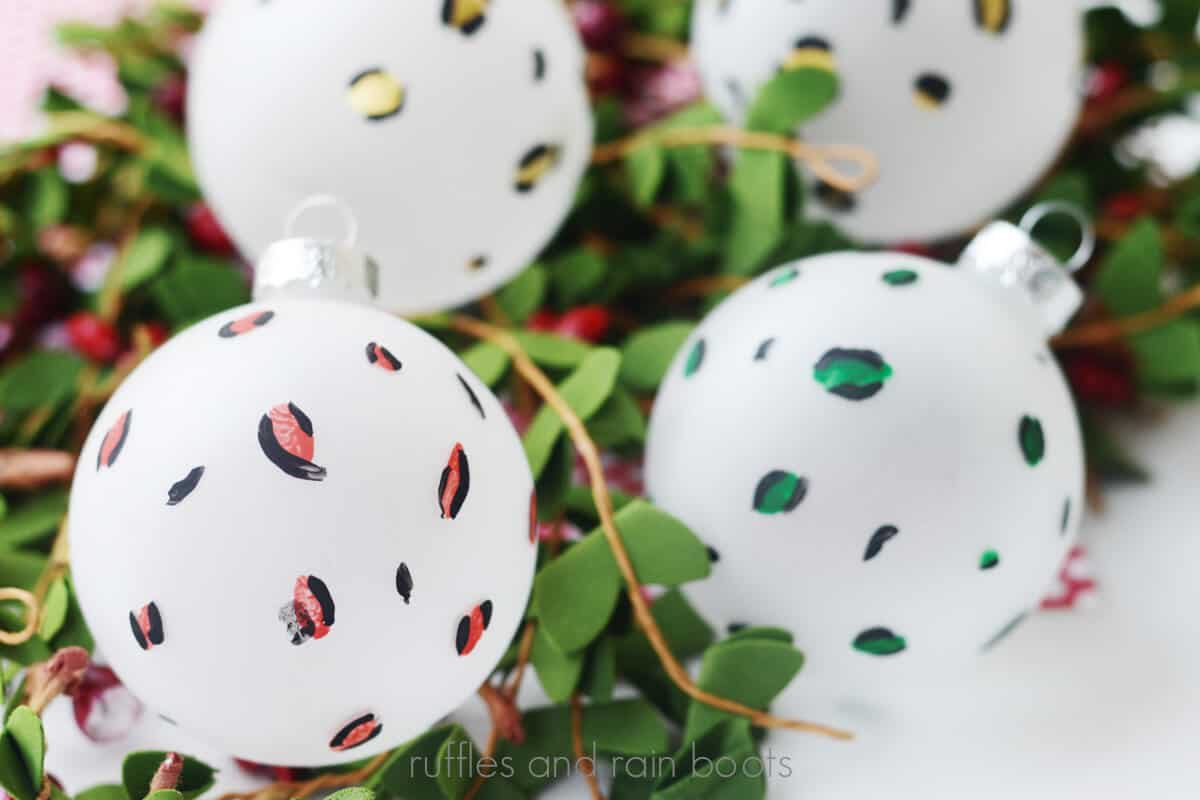 Horizontal image of four, colorful animal print or leopard print Christmas ornaments on a bed of faux holly and berries.