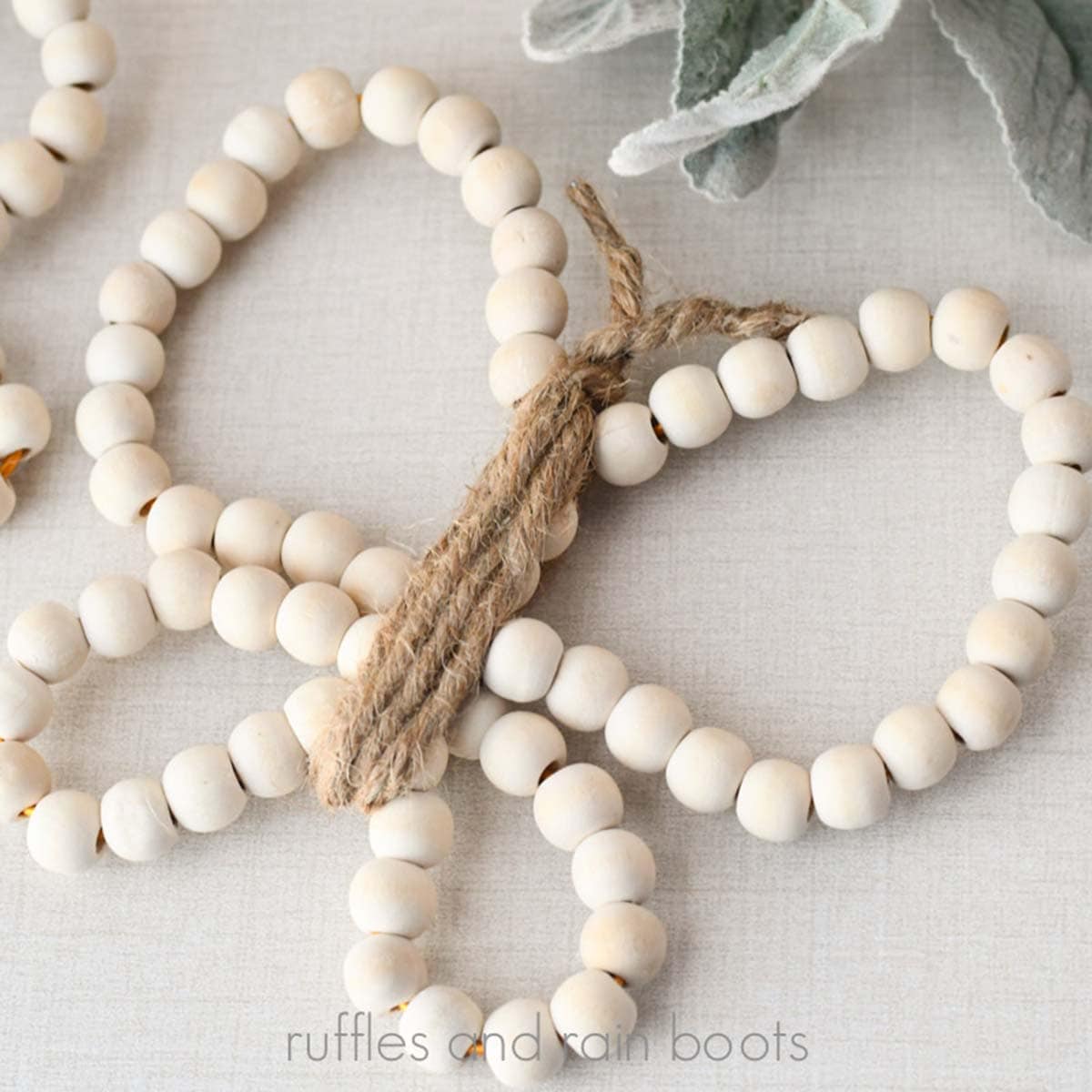 Close up square image of a wood bead butterfly with twine body and antennae on linen background with leaves.