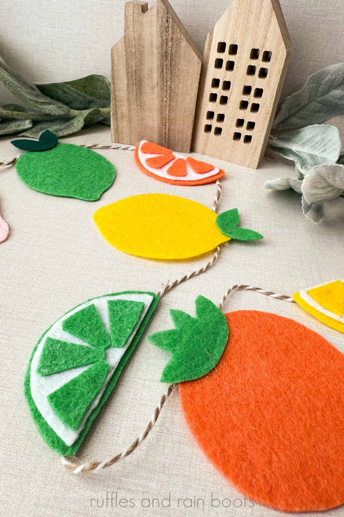 Vertical close up image of fruit made of brightly colored felt and strung onto a garland.