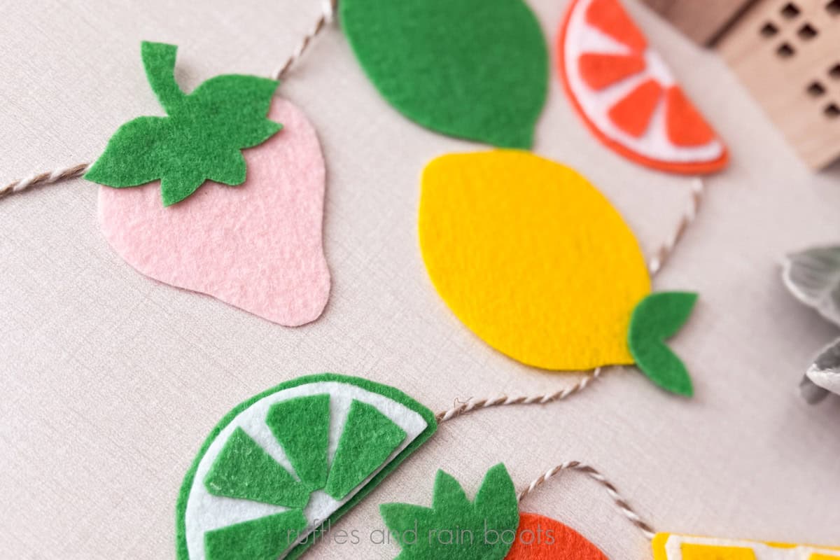 Horizontal close up image of felt fruit made into a garland for a summer party.
