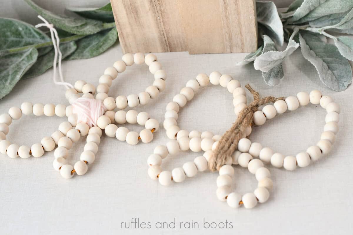 Horizontal image of a pair of wooden bead butterflies with yarn and twine on a linen background with lamb's ear and wood accents.