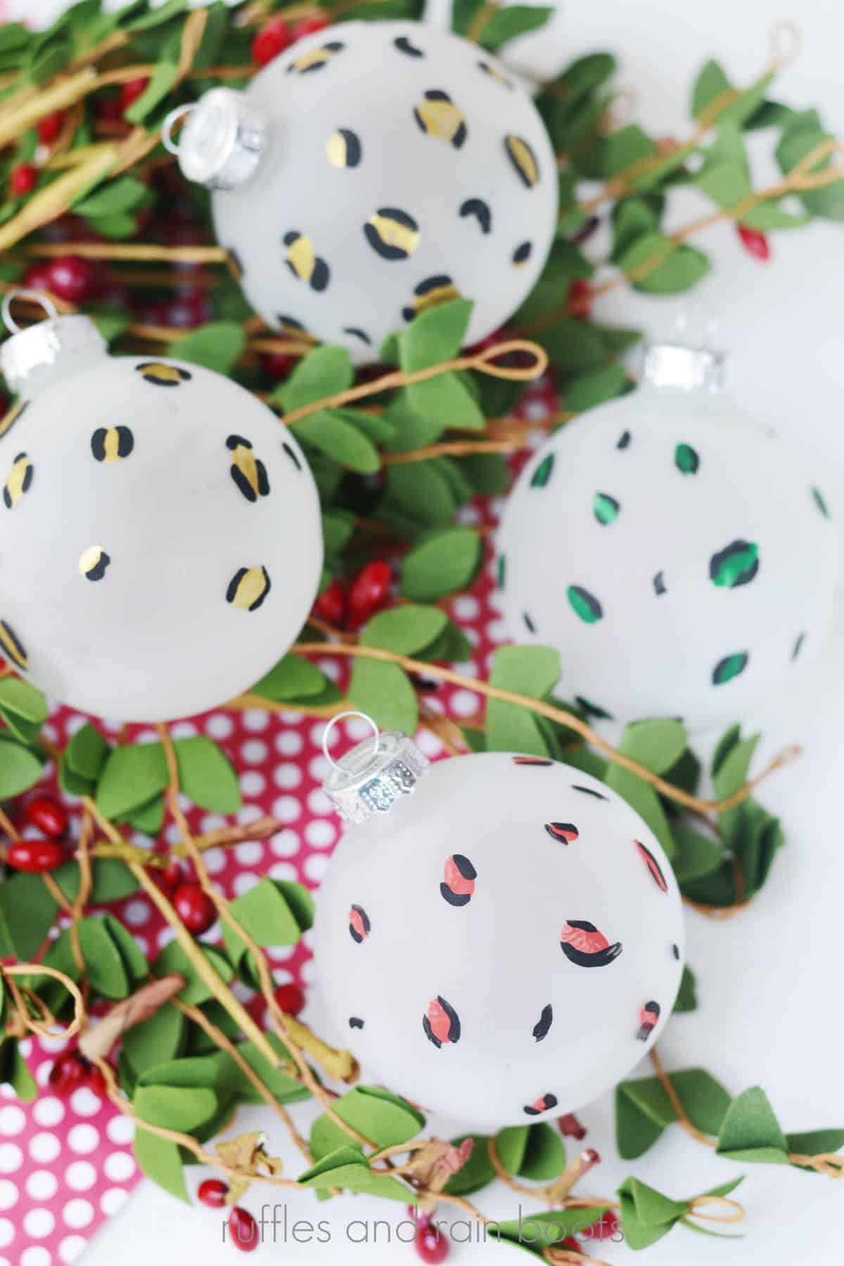 Vertical image of red, green, and gold leopard print painted Christmas baubles.