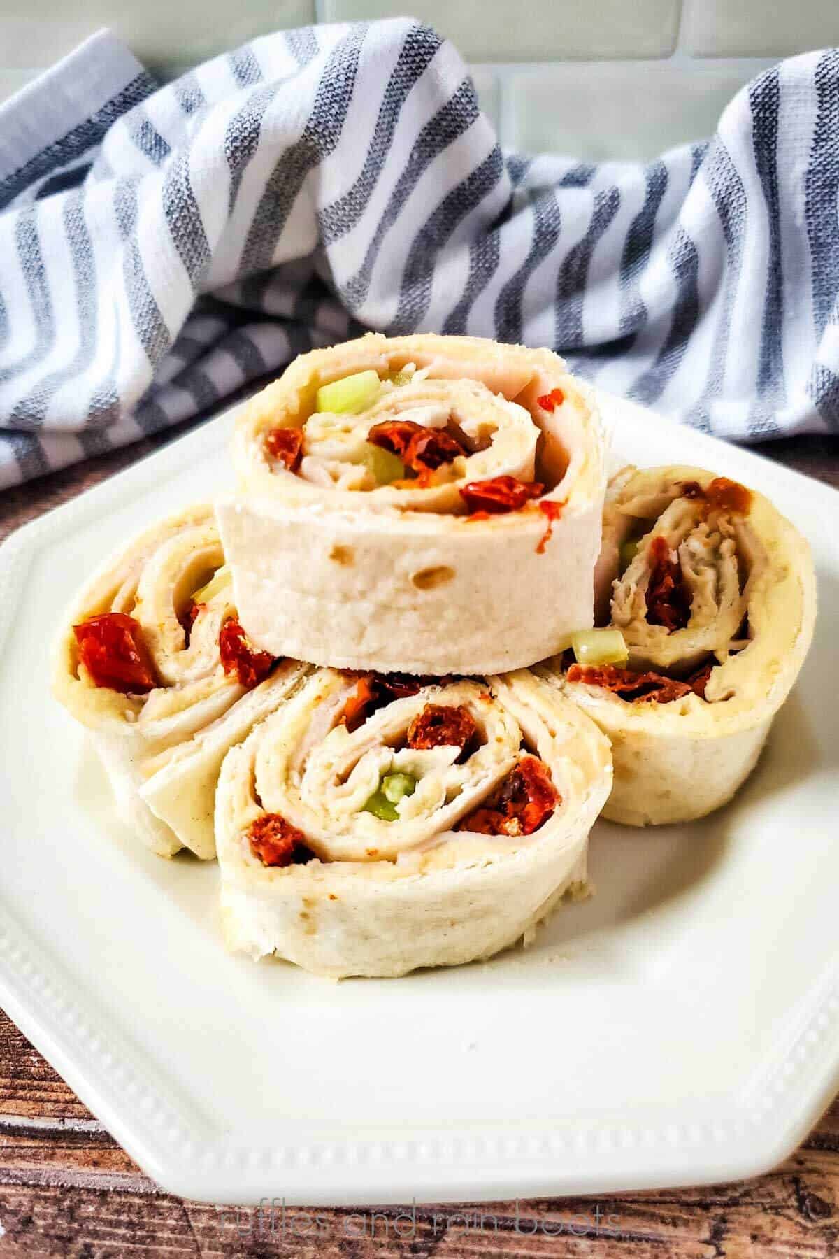 Vertical image of turkey and sun dried tomatoes stacked on a white plate in front of a striped towel.