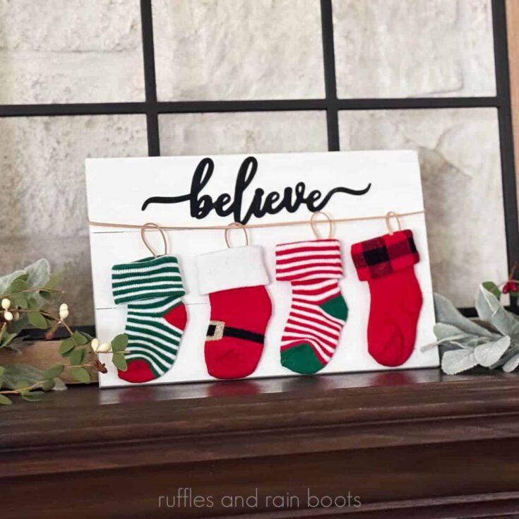 Horizontal image of four colorful holiday baby socks strung on a cord and placed onto a wood plank as a Christmas decoration.