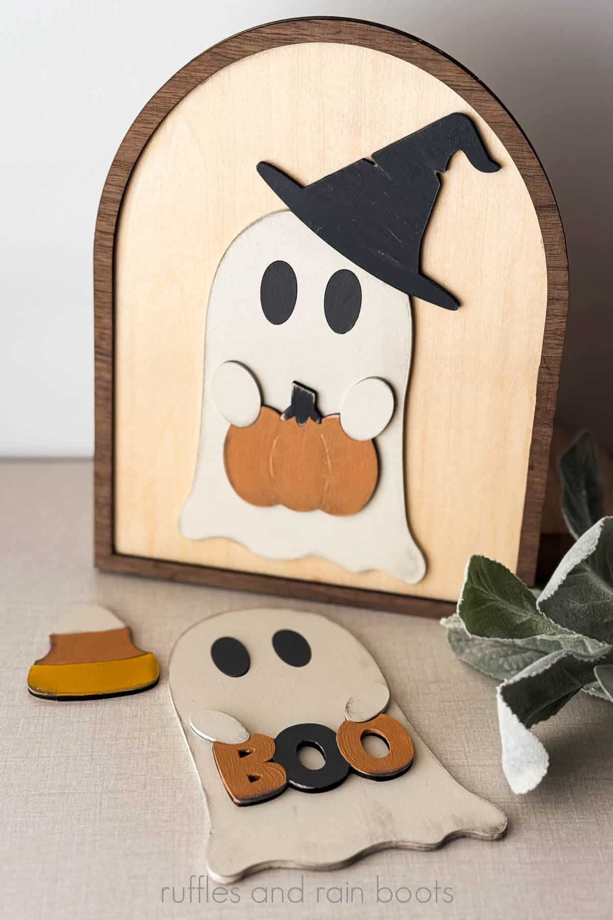 Vertical image of a ghost wearing a black witch hat holding an orange pumpkin with a second ghost holding a BOO sign.