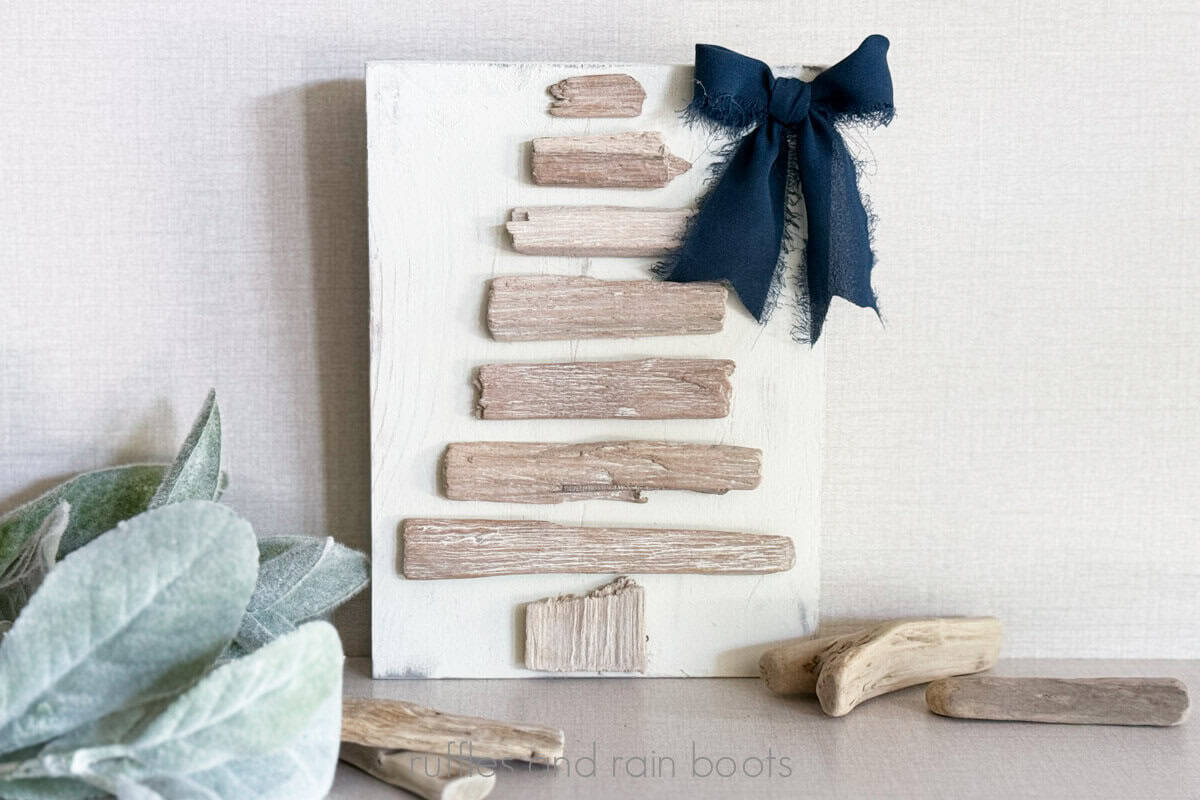 Horizontal close up image of a driftwood Christmas tree on a painted wood board with a beachy scene.