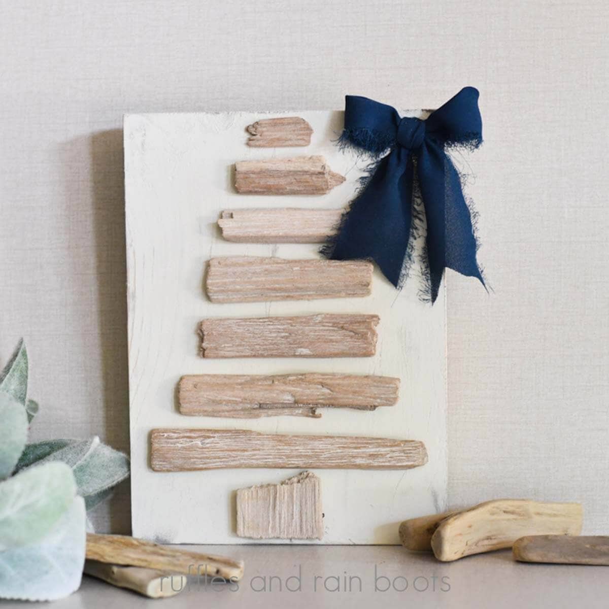 Square image of a Christmas tree made of driftwood pieces and a navy bow.