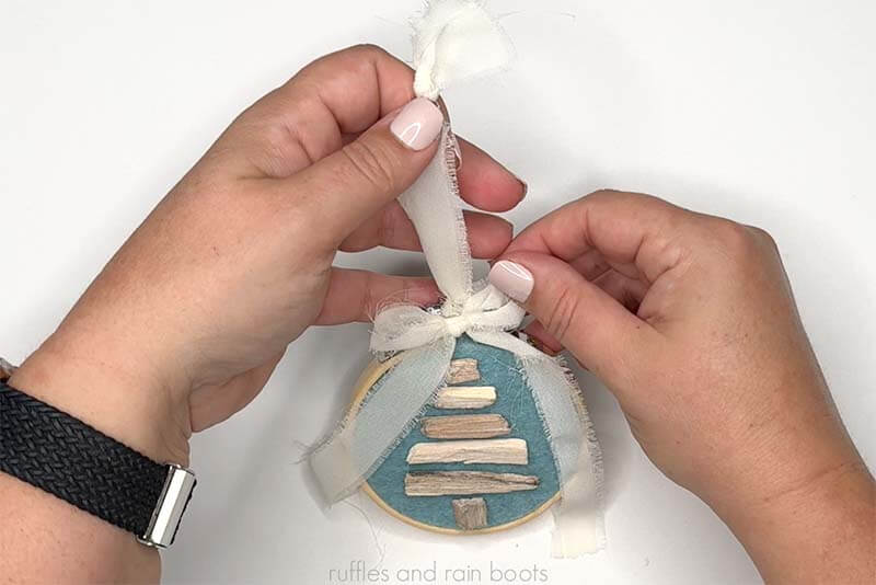 Crafter adding a cream chiffon ribbon to the driftwood Christmas tree craft.