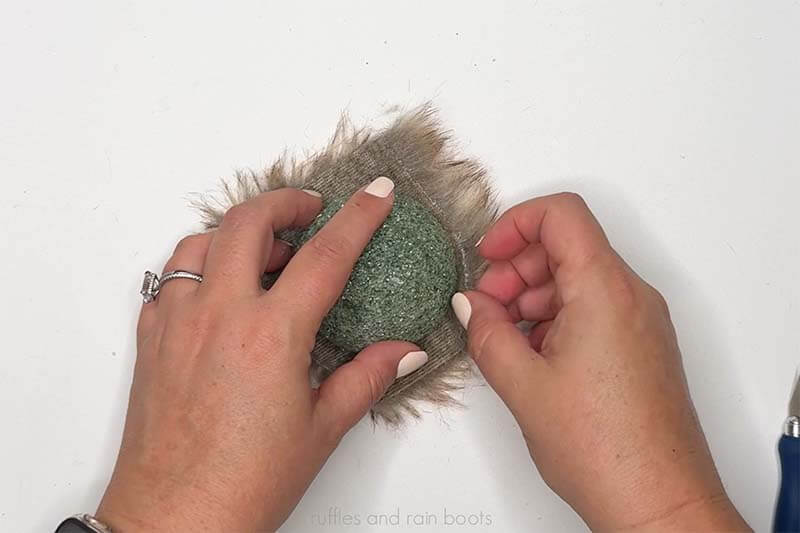 Crafter adding faux fur to cover half of a Dollar Tree foam ball.
