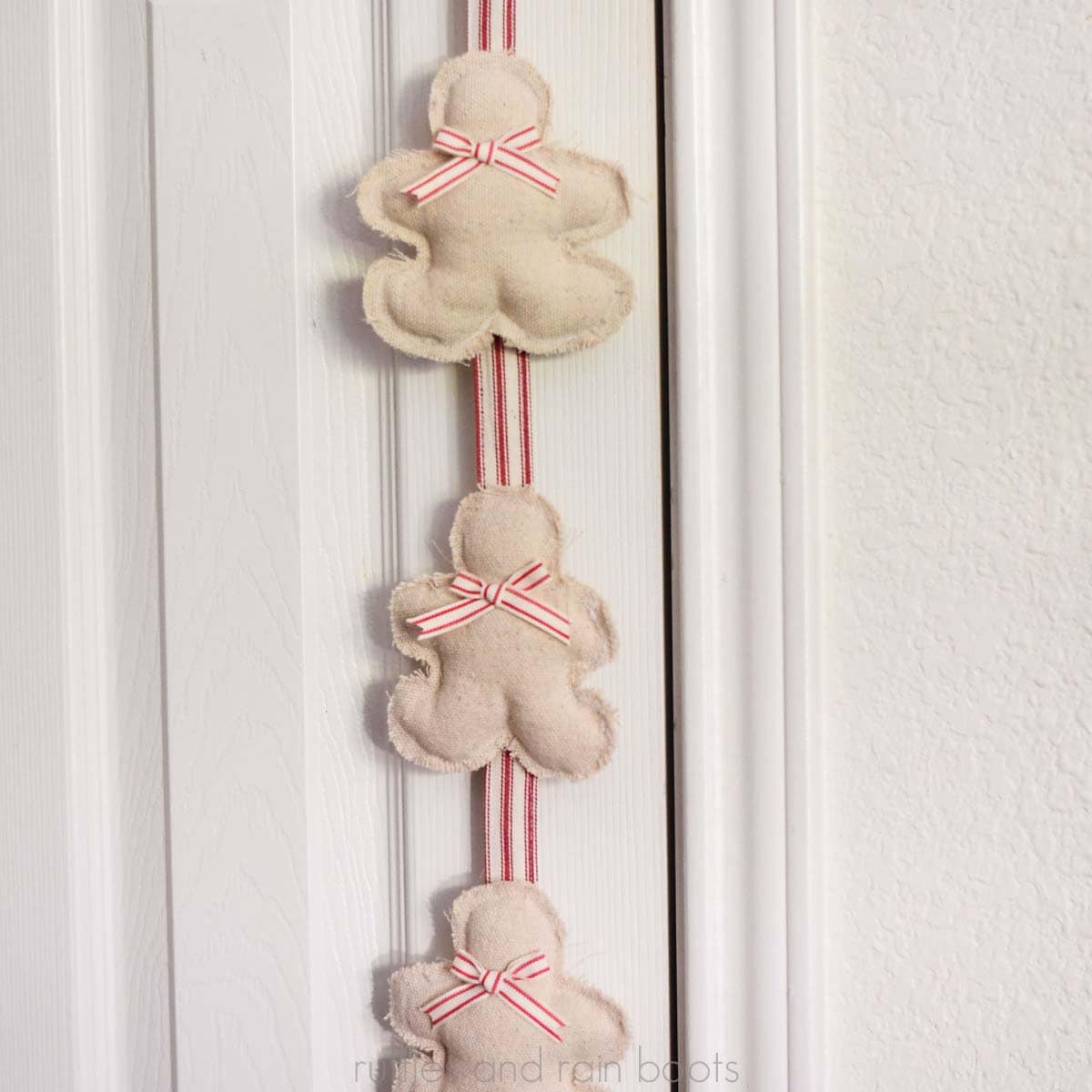 Square, close up image of three gingerbread men hanging on a Christmas door knob garland as part of a holiday gingerbread kitchen design.