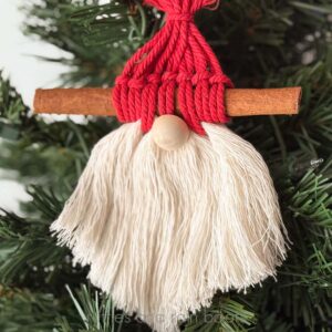 Square up close image of a Santa gnome ornament made with macrame cord and a cinnamon stick.