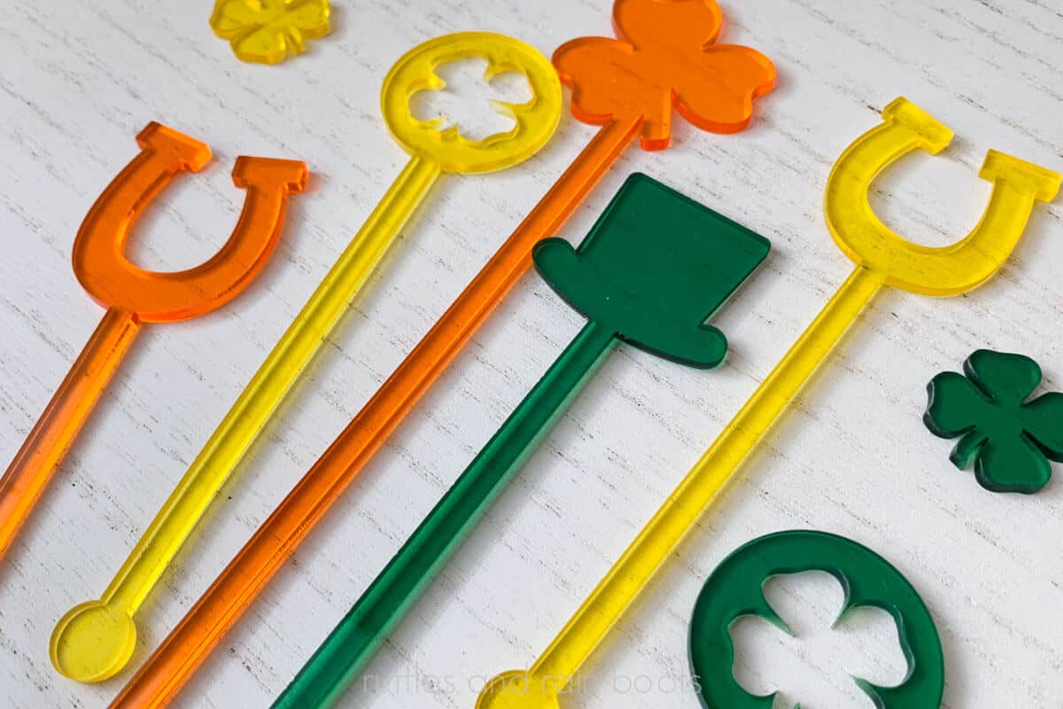 Horizontal image of orange, yellow, and green translucent acrylic stir sticks on a white wood background.
