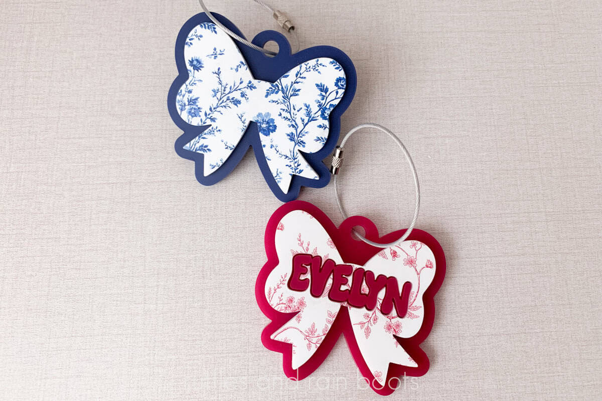 Horizontal close up image of two adorable bow bag tags in a coquette style, made with two colors of acrylic.
