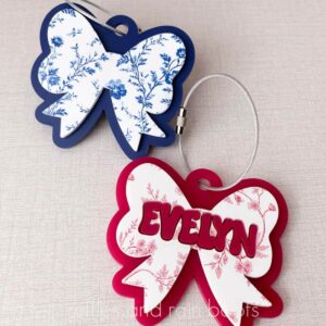 Square, close up image of a blue and white and a pink and white acrylic bow bag tag charms with wire cables for purses, bags, and backpacks.