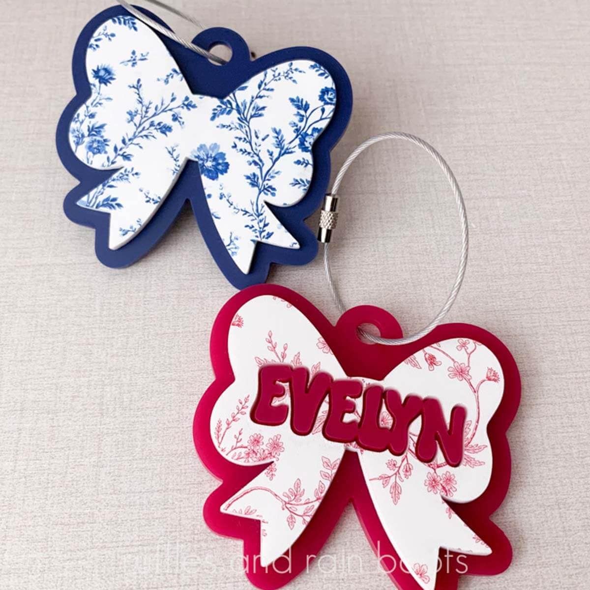 Square, close up image of a blue and white and a pink and white acrylic bow bag tag charms with wire cables for purses, bags, and backpacks.