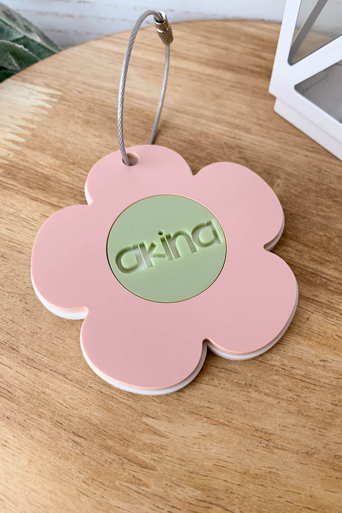 Vertical close up image of a pink, green, and white daisy bag tag with a wired tag for back packs.