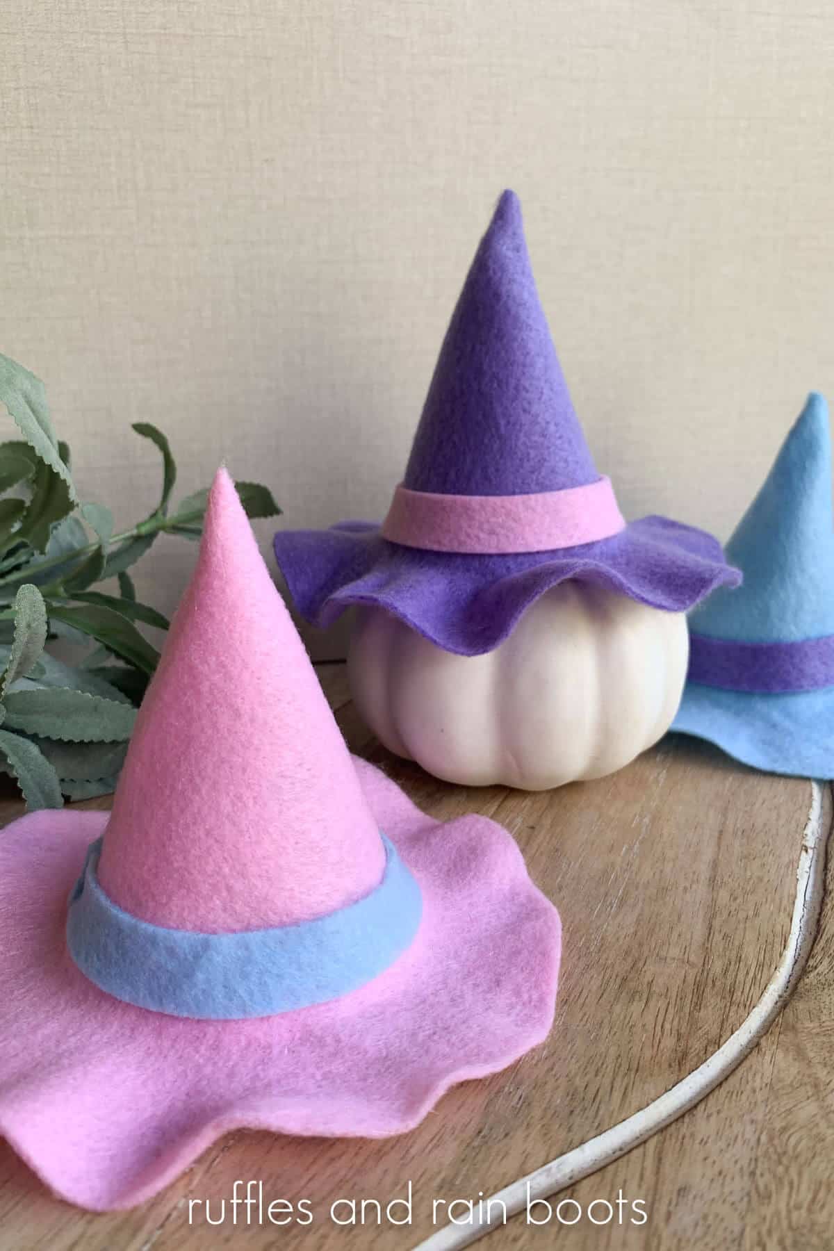 Vertical image of a pink, purple, and blue mini witch hat selection on top of a pumpkin for a cute Halloween display.