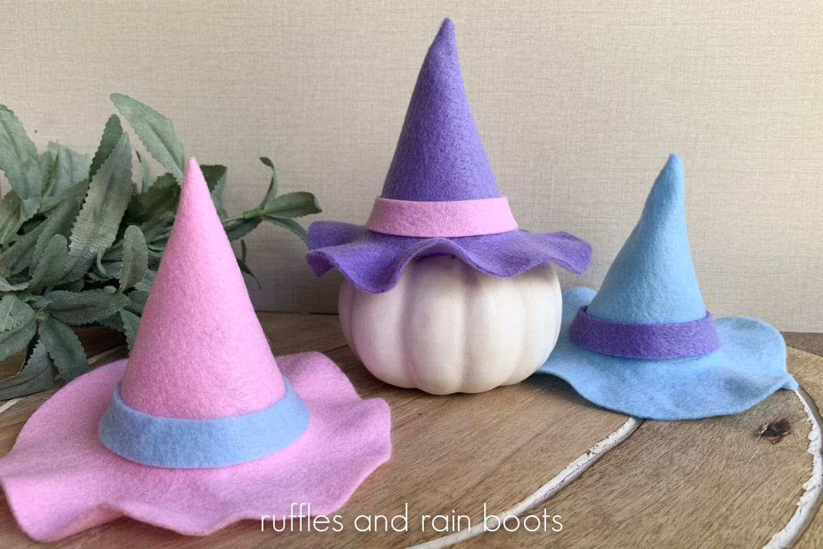 Horizontal image of three mini witch hats made from pastel felt in front of a linen background with small greenery.