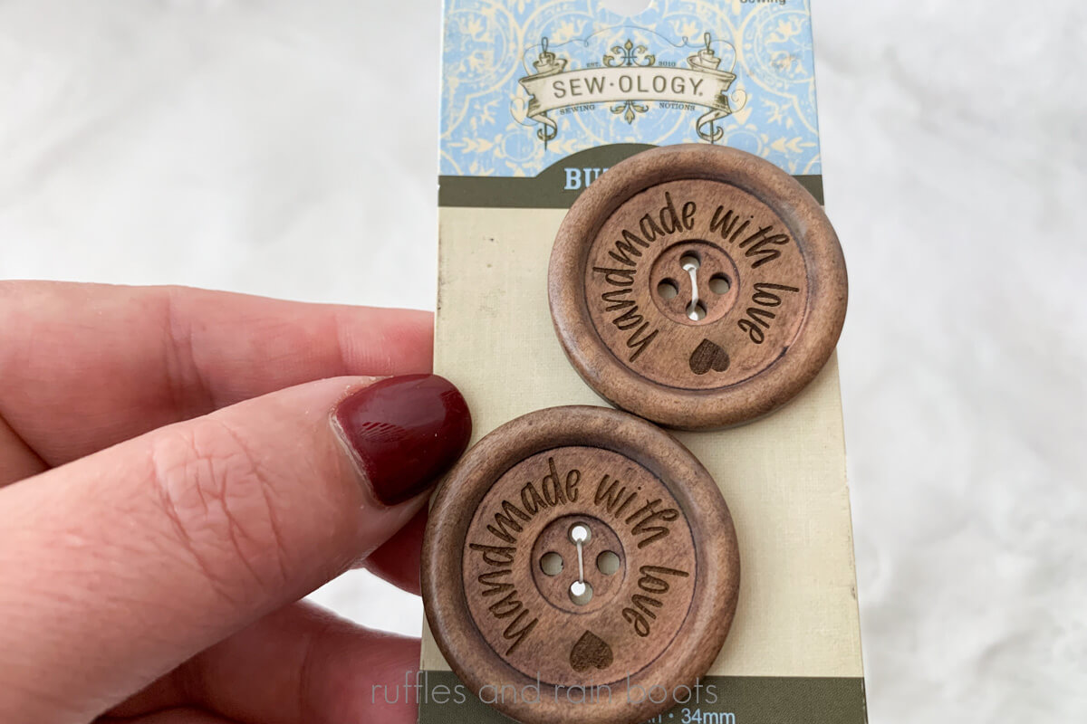 Close up horizontal image of a woman's hand holding packaged and engraved wooden buttons which read handmade with love.