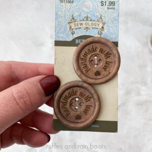 Square close up image of two laser engraved wooden buttons which reads handmade with love and an engraved heart.