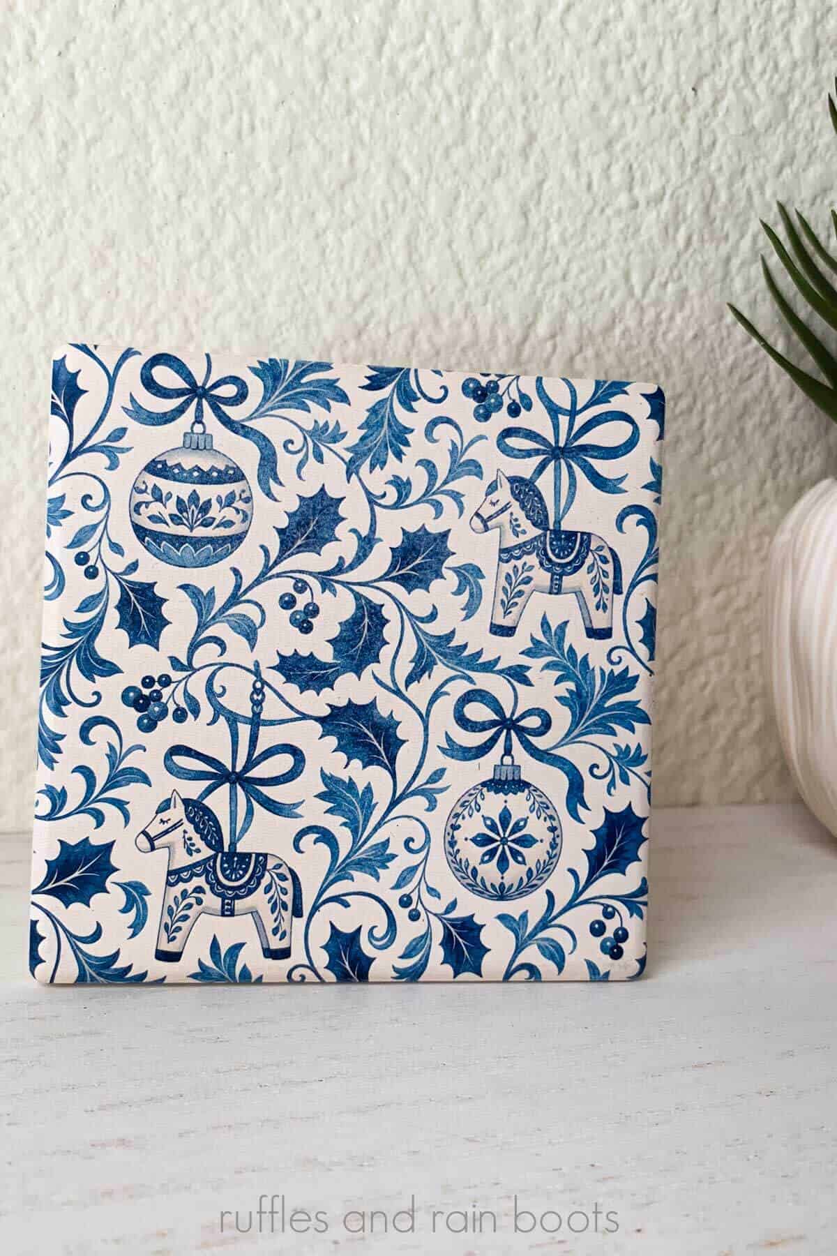 Vertical image of a blue and white toile inspired Christmas coaster set with ornaments, Dala horses, and bows.